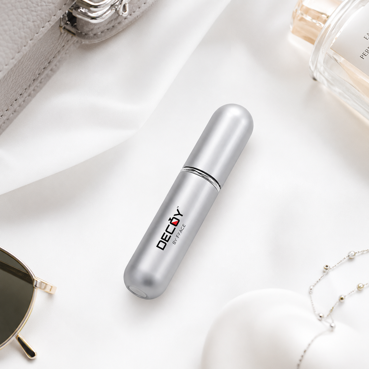 Silver cylindrical container with 'Decoy' branding on a white surface with sunglasses and a perfume bottle.