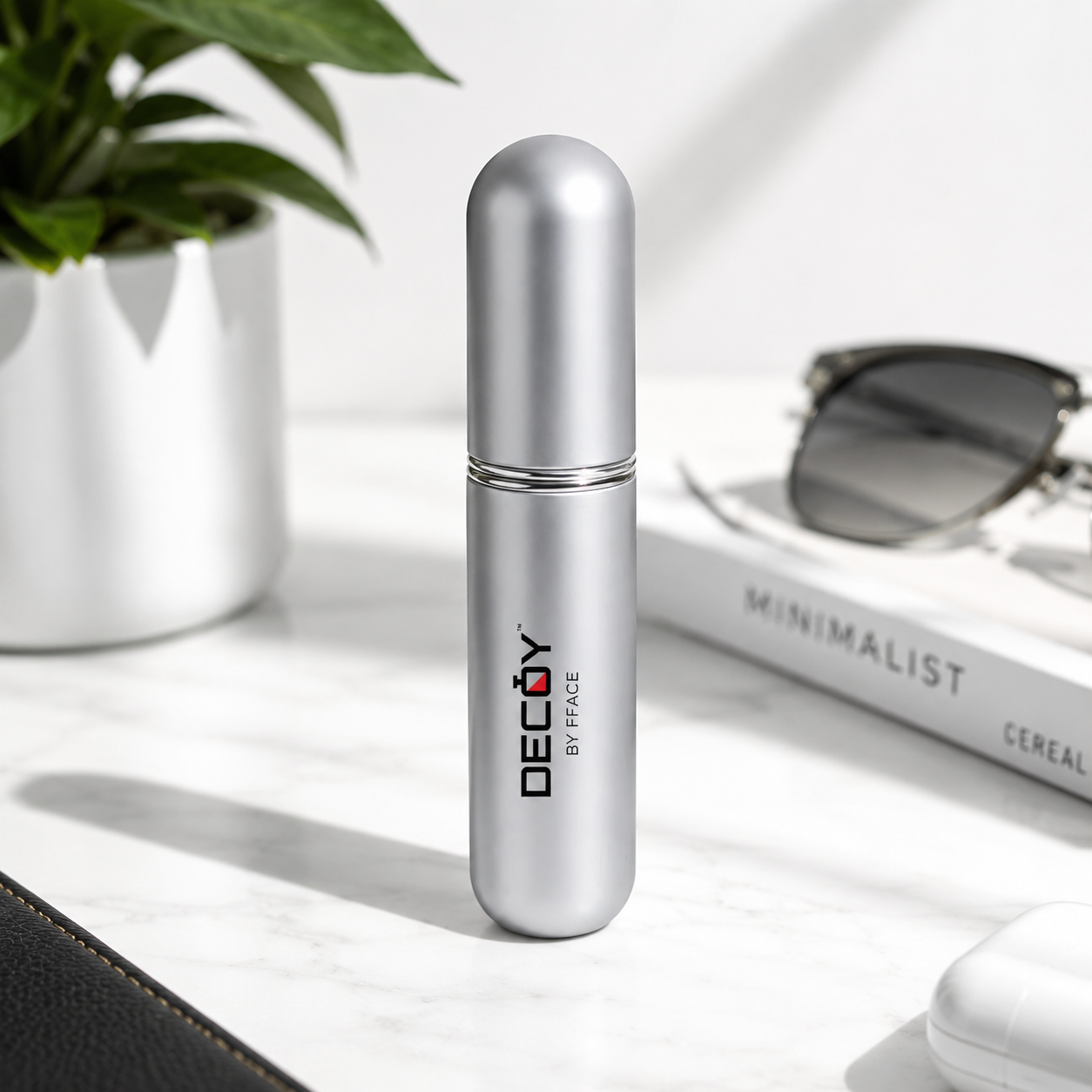 Silver cylindrical container with 'DECOY by FACE' branding on a light surface with sunglasses and a plant in the background.