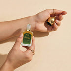 Hand holding a decoy luxury asrar attar oil bottle against a beige background