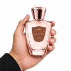 Hand holding a pink perfume bottle labeled 'Oud Affair' with a rose gold cap on a white background.