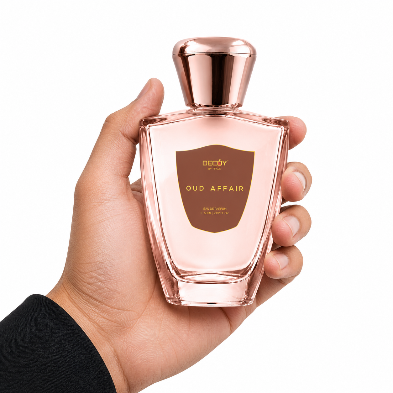 Hand holding a pink perfume bottle labeled 'Oud Affair' with a rose gold cap on a white background.