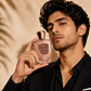 Man holding a perfume bottle labeled 'Oud Affair' against a beige background