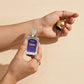 Hand holding a bottle of 'Zahoor' aftershave with a gold bell on a beige background